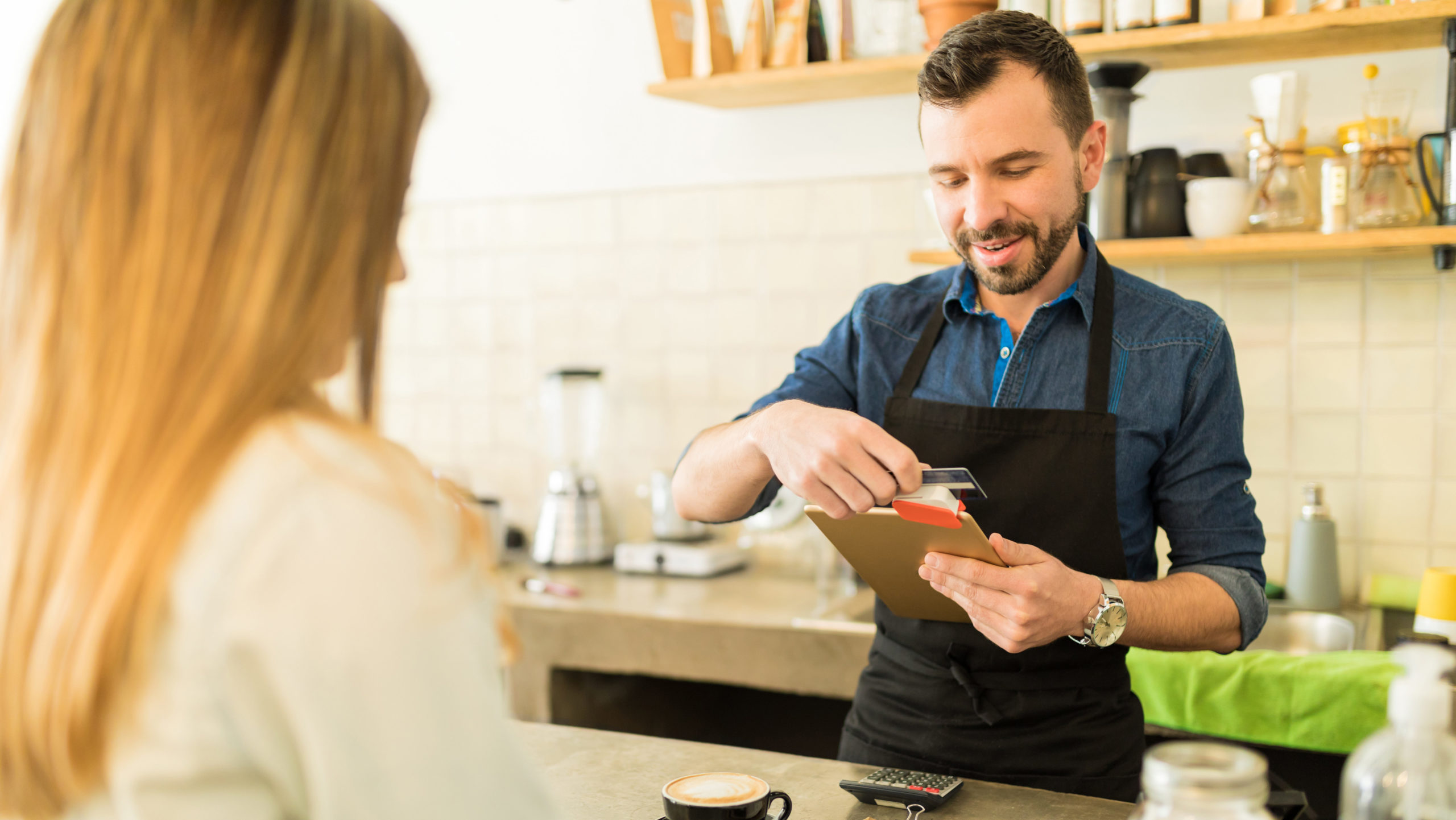 Customer paying for coffee at a cafe while barista swipes her credit card